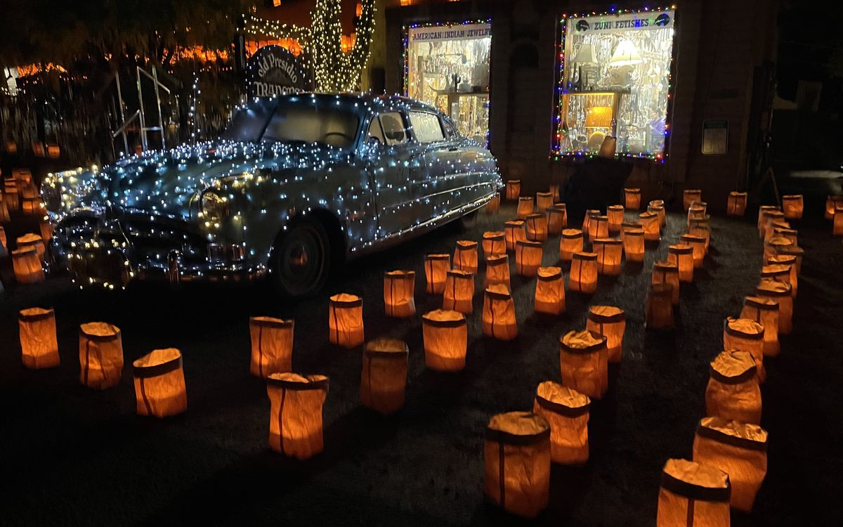 Hileras de luminarias de bolsas de papel encendidas frente a Old Presidio Traders en Tubac, junto a un auto antiguo cubierto de series de luces blancas